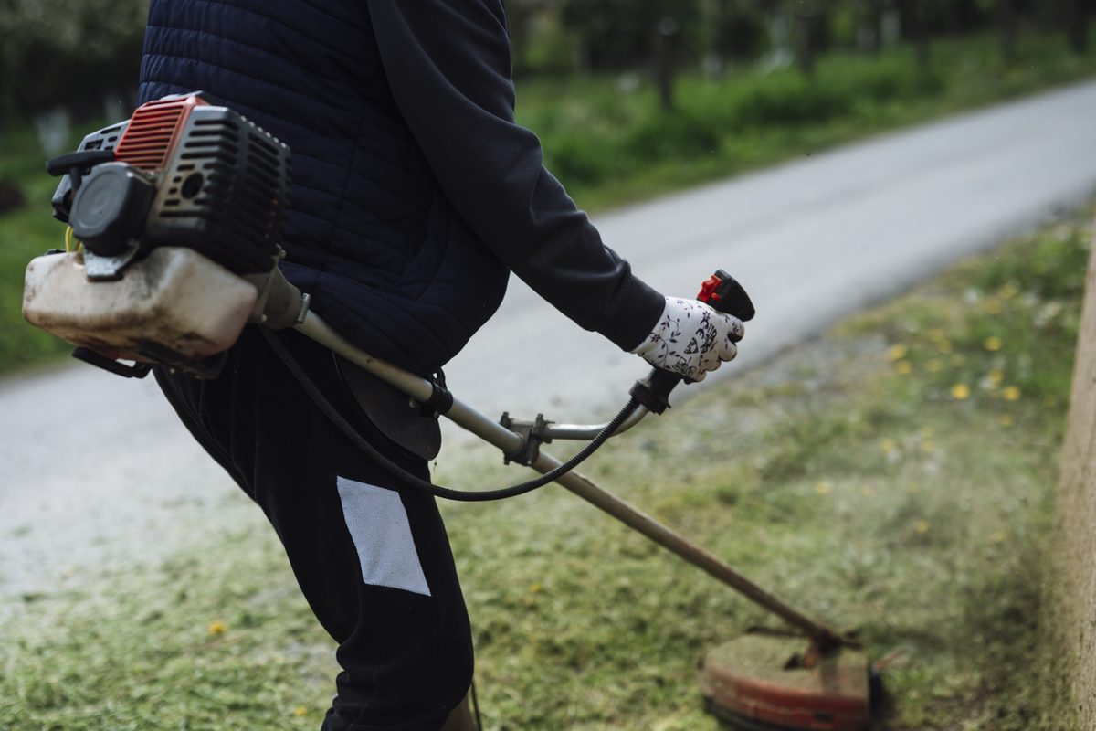 Worker trimming grass along a path with a string trimmer